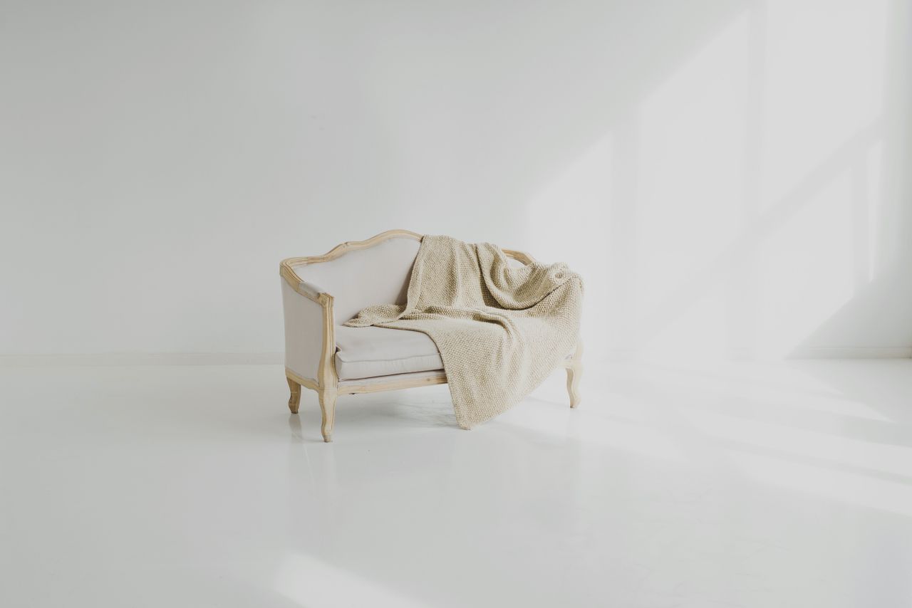 services-04 A beige throw on a vintage white sofa in a bright minimalist living space.